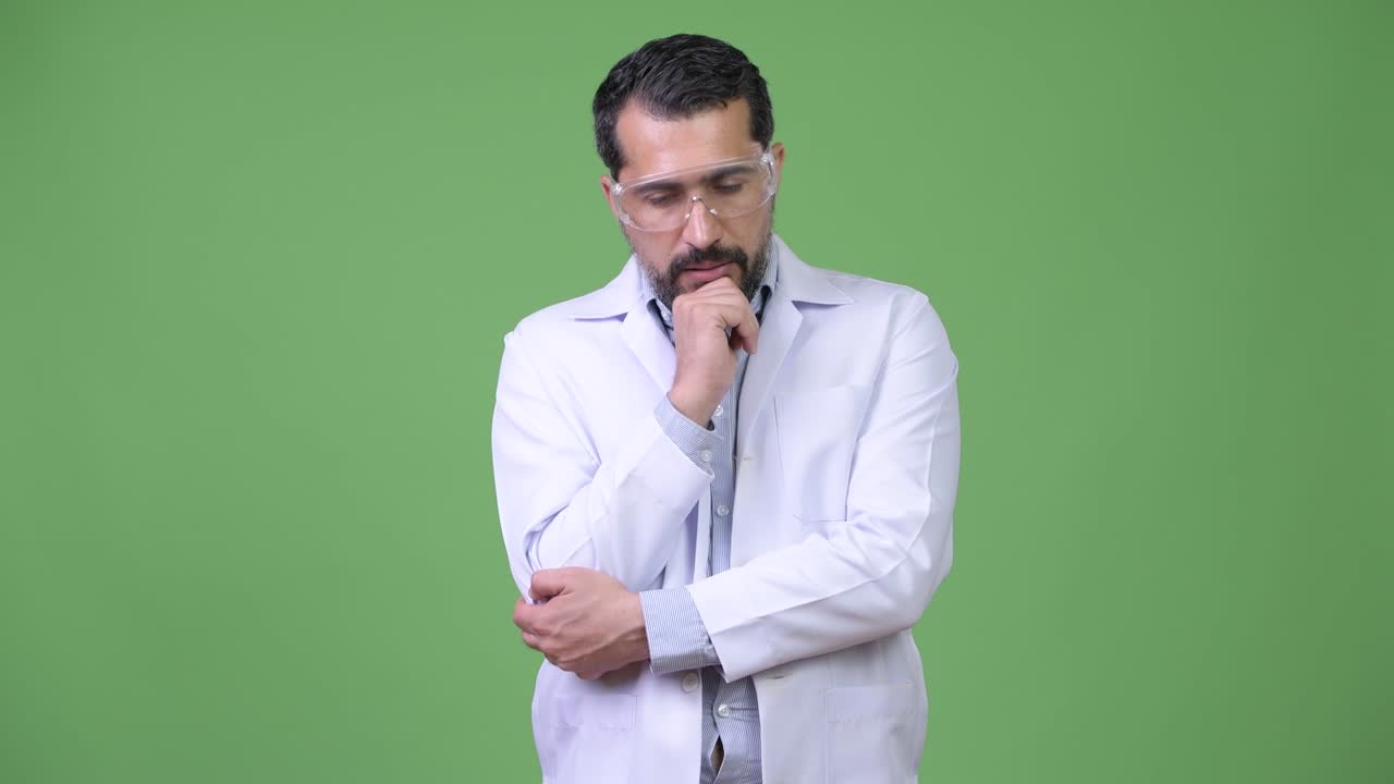 Serious Persian bearded man doctor wearing protective glasses while thinking