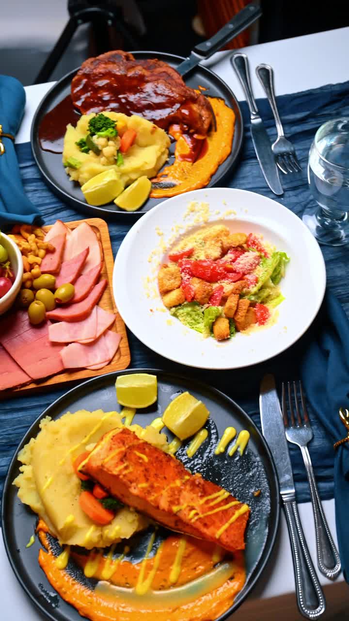 Vista dall'alto di una cena con più portate, con salmone, aragosta e insalata. Vista dall'alto di vari piatti gourmet disposti su un tessuto blu testurizzato.