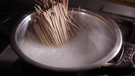 adding japanese soba noodles to hot water, making asian noodle dish