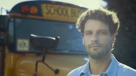 Confident-man-driver-stand-at-yellow-bus-looking-camera-in-sunlight-close-up.