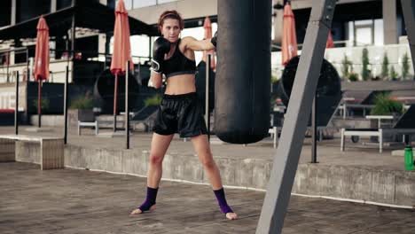 Boxeadora-Haciendo-Ejercicio-Al-Aire-Libre.-Hermosa-Mujer-Atlética-Con-Guantes-Golpeando-Una-Bolsa-Afuera.-Concepto-De-Autodefensa.-Camara-Lenta