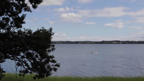 happy people sailing in canoes on the windy water lake with clouds and trees in the background