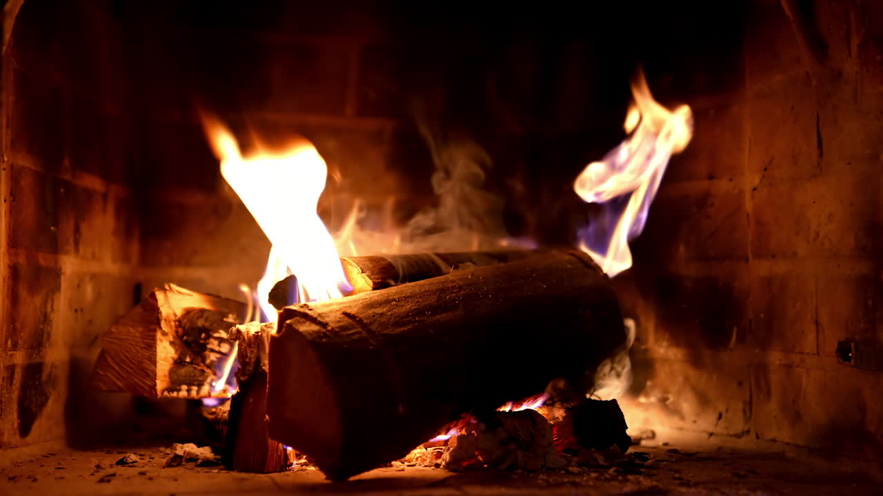 Wooden logs in fire on brick fireplace background. Wood burning in fire flame. Cozy warm fireplace in a country house. Close-up.