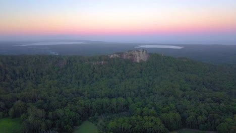 rising aerial view of mount tinbeerwah at sunset with tropical forest, ocean and pink sky