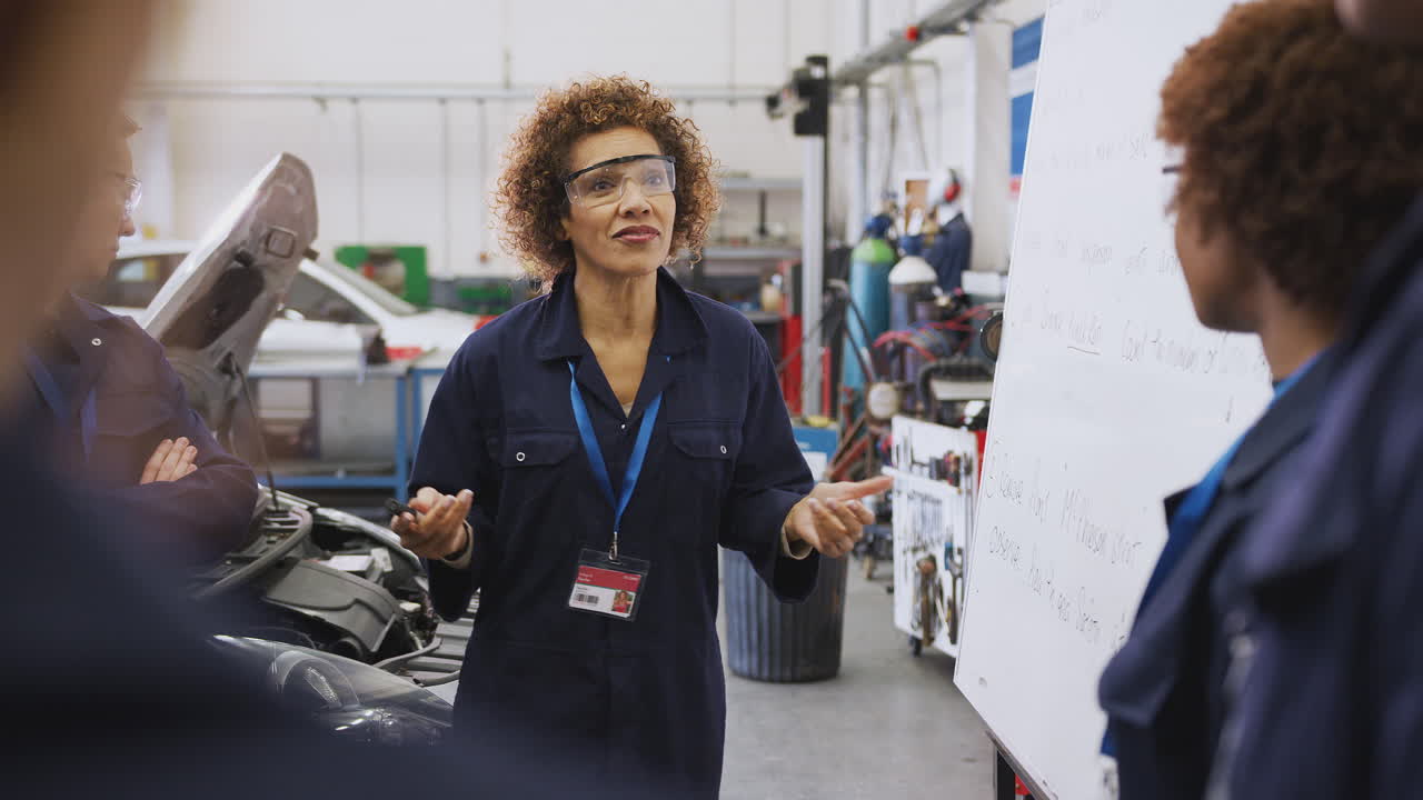 Female Tutor By Whiteboard With Students Teaching Auto Mechanic Apprenticeship At College