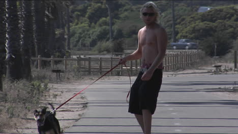 a man walks a dog while skateboarding