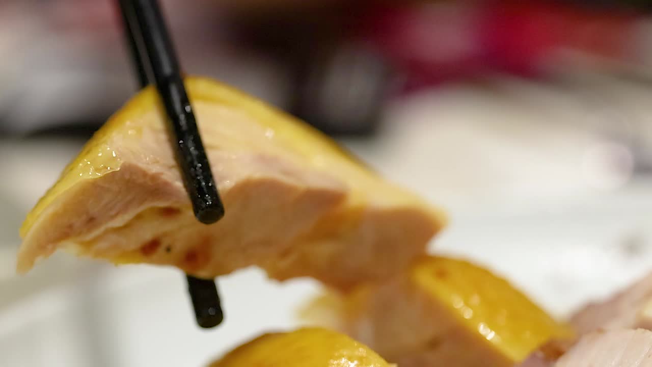 Scatto macro di bacchette nere che sollevano un pezzo di succulento pollo arrosto da un piatto.