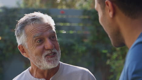 Senior-Hispanic-Man-Talking-And-Laughing-With-Adult-Son-In-Garden-At-Home