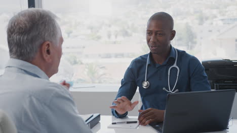 Senior-Male-Patient-In-Consultation-Shaking-Hands-With-Doctor-Sitting-At-Desk-In-Office