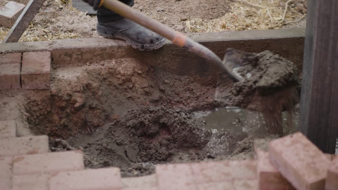 Construction workers use shovels to apply cement mixture to building support pillars