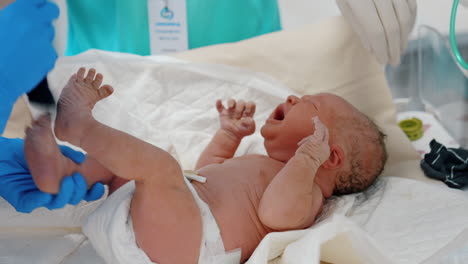 tiny newborn baby is being undressed by medics. child is unhappy and cries waving hands. close up.