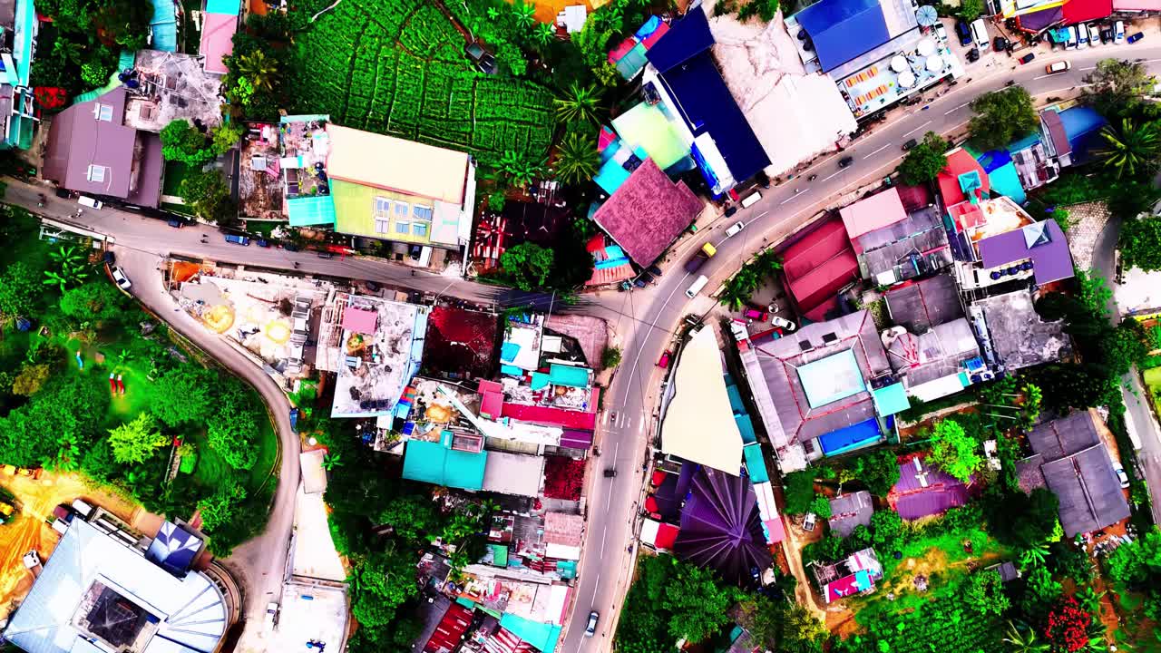A vivid aerial captures a Sri Lankan village with colorful rooftops, narrow winding roads, and dense building clusters surrounded by green tropical vegetation and lively local textures.