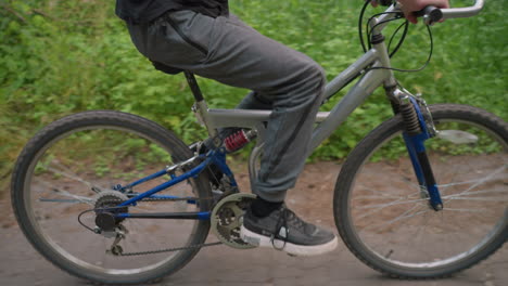 side view of cyclist riding along an untarred path surrounded by lush greenery, the cyclist is wearing grey trousers and sneakers while enjoying a leisurely ride in nature