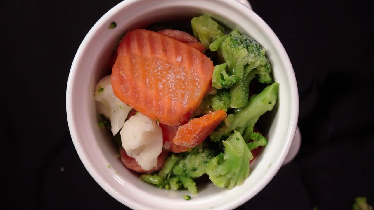 Colorful frozen vegetables in a white bowl on a dark surface