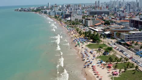 rising aerial shot of intermares beach in cabedelo, brazil with brazilians and tourists enjoying the ocean near the costal capital of joao pessoa in the state of paraiba on a warm sunny summer day
