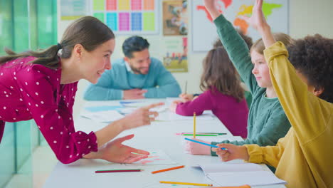 group of multi-cultural students putting hands up to answer question in classroom lesson