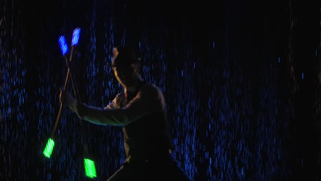 man juggling with illuminated props in a dark rainstorm