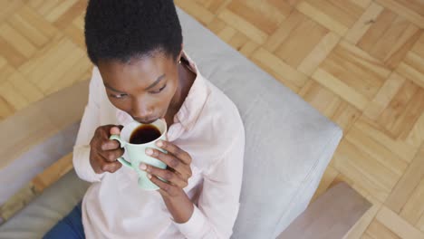 Glückliche-Afroamerikanische-Frau-Sitzt-Auf-Einem-Sessel-Im-Wohnzimmer-Und-Trinkt-Kaffee