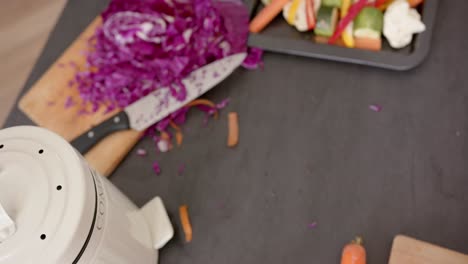 Close-up-of-countertop-with-chopping-board,-knife-and-chopped-vegetables-in-kitchen,-slow-motion