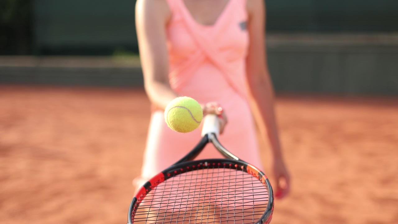 Close-up of a Woman Bouncing a Tennis Ball on a Racket on a Clay Court