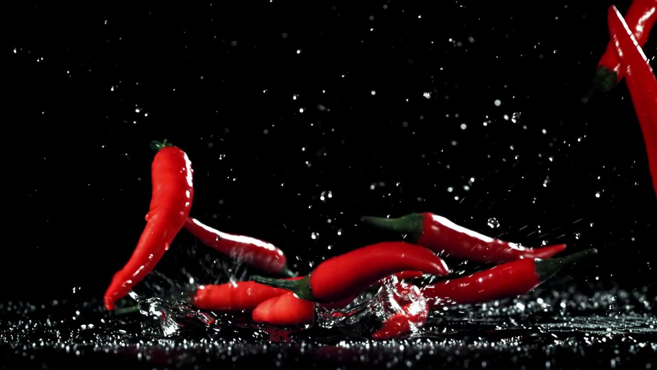 Røde chilipepper faller og spruter på våt overflate i sakte film