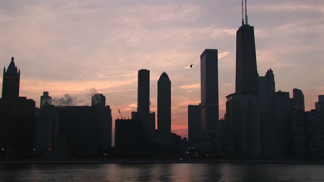 A Goldenhour Chicago Skyline With Silhouetted Buildings Against A Pink And Orange Sky