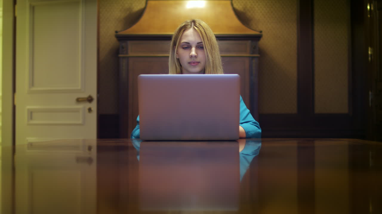 Ernsthafte Frau, die an einem Notebook-Computer arbeitet und am Tisch im Heimstudio sitzt