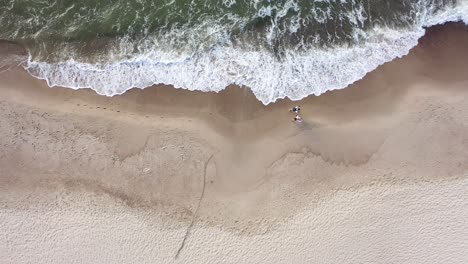 aerial: top view of couple walking on a cloudy day on beach with bare foots