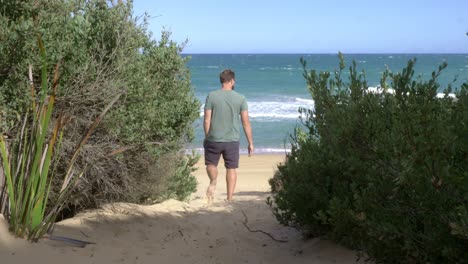 macho caminando descalzo por la pista de arena hacia la playa ventosa olas del océano