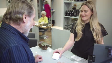 senior man making contactless payment to stylist in salon with credit card