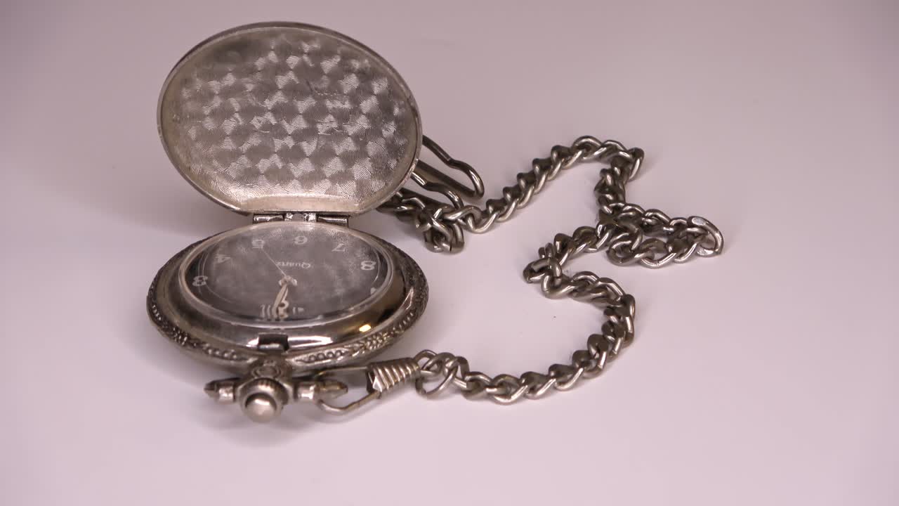 un viejo reloj de bolsillo abierto en una cadena de plata gira lentamente en un círculo.