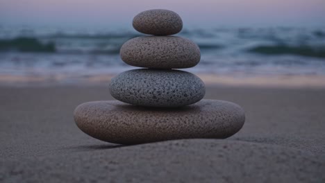 A serene video of stacked stones on a beach at sunset, captured from a low angle