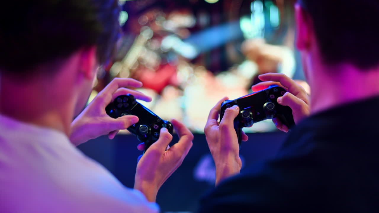 CHISINAU, MOLDOVA - SEPTEMBER 9, 2023: Two teen friends are playing a game console using gamepads, close view of hands, TV on the background. Blue and red illumination