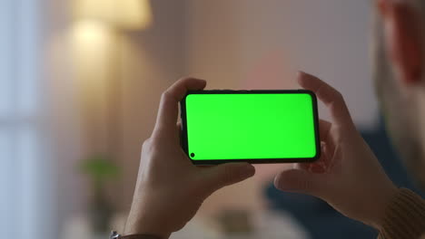 un hombre está viendo cine en un cine en línea usando un teléfono inteligente con sensor táctil, pantalla verde, tecnología de entretenimiento en el hogar durante el fin de semana y el aislamiento.