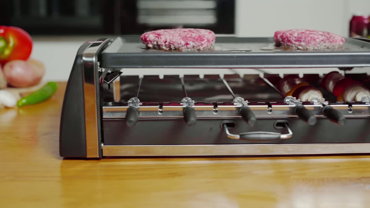 Useful plancha grill searing burgers, spinning skewers. Sideways pan, closeup