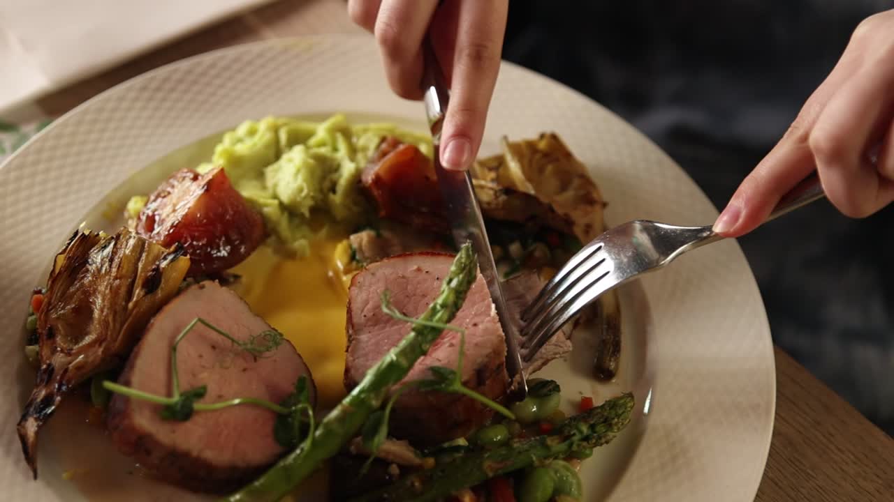 Nahaufnahme von Händen, die ein Gourmet-Schweinefiletgericht schneiden