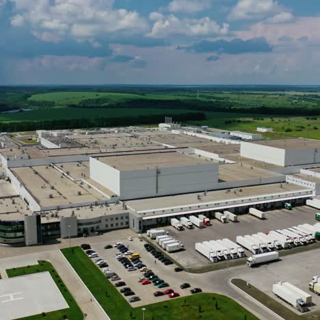 manufacture zone in nature. modern territory of huge industrial complex with car parking surrounded by green landscape. aerial view. camera moves back.