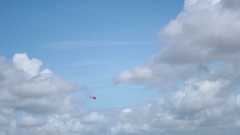 red helicopter against blue sky and clouds