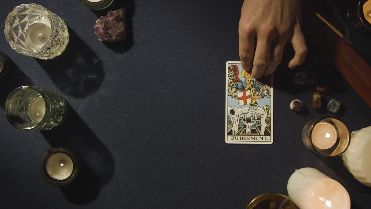 toma aérea de una persona que da una lectura de cartas del tarot colocando la carta de juicio en la mesa