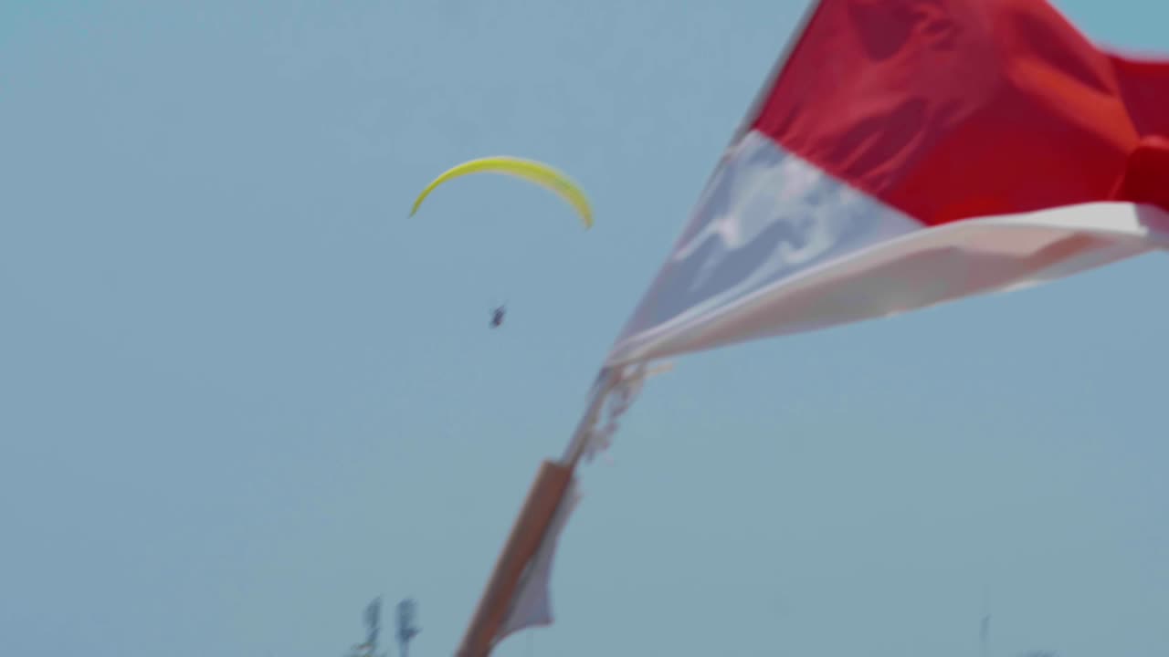 La bandiera indonesiana sventola mentre un parapendio vola sullo sfondo.