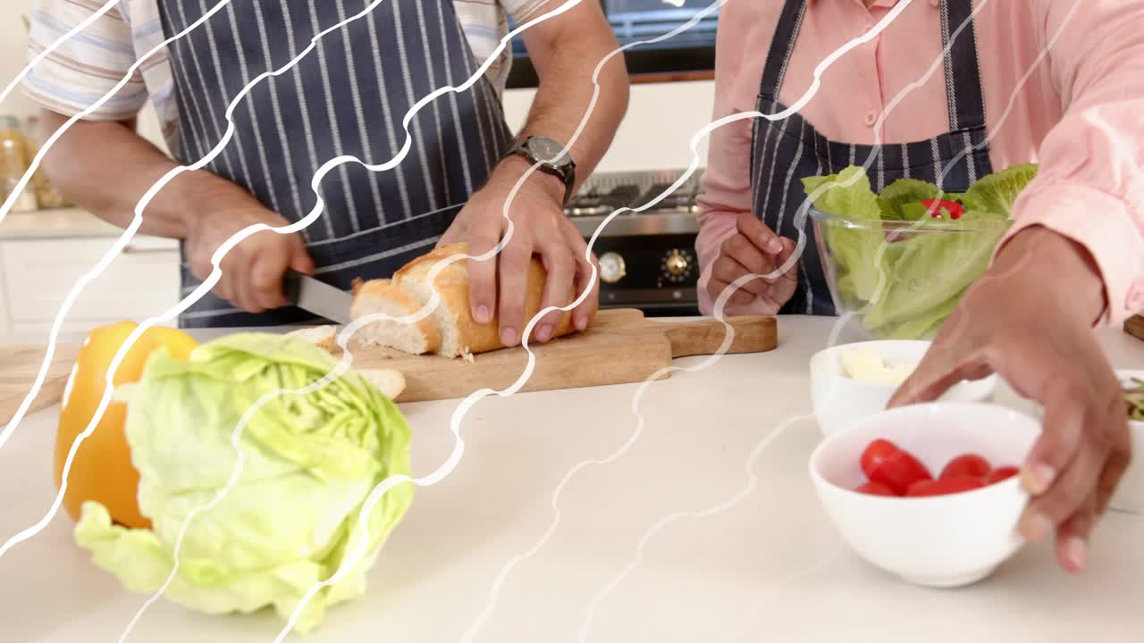 Man and woman preparing meal at counter, man starting slicing loaf while woman holding salad bowl