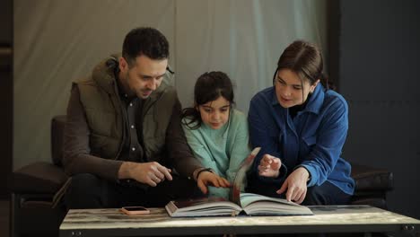 Looking Through Snowy Window. Happy Family: Father, Mother and Their Little Daughter are Decorating. Looking Through Snowy Window. Happy Family: Father, Mother and Their Little Daughter are Decorating Christmas Tree