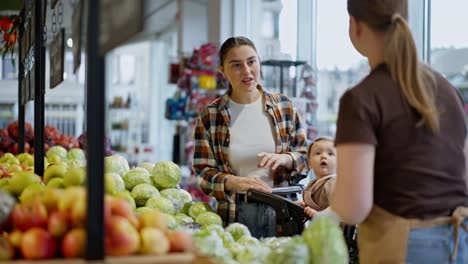 una feliz chica morena se acerca a un trabajador de un supermercado y le pregunta sobre las verduras en el mostrador durante su compra con su hija