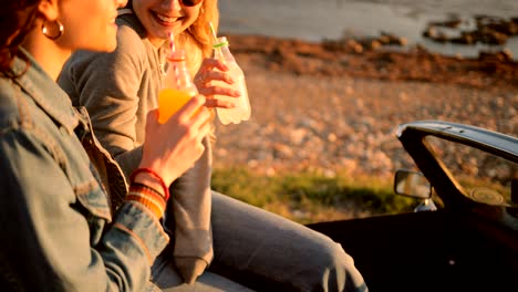 hipster women in retro convertible car drinking soda at beach