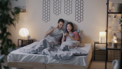 pareja relajándose en la cama con un teléfono inteligente