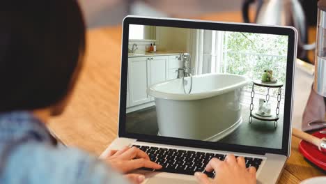 woman using laptop with modern bathroom interiors displayed on screen