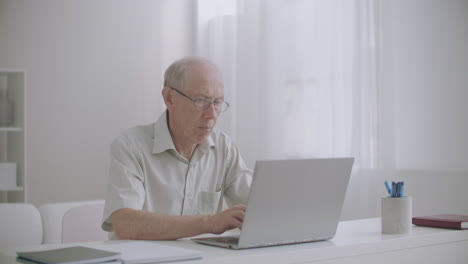 Un-Anciano-Independiente-Está-Trabajando-Desde-Casa-Con-Una-Computadora-Portátil.-Un-Escritor-Anciano-Está-Escribiendo-Un-Libro-Escribiendo-Texto-En-El-Teclado.