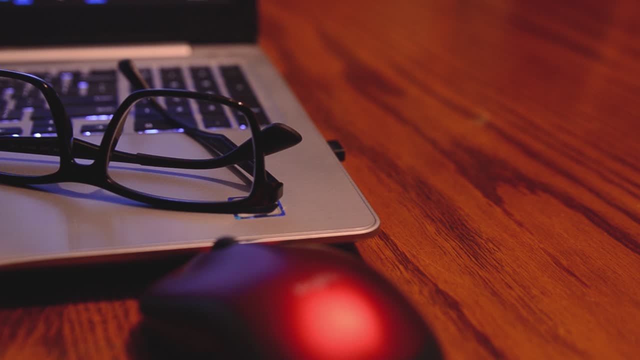 노트북 컴퓨터 위에 놓여 있는 안경의 왼쪽에서 오른쪽으로 이동하는 슬라이더 샷이 마우스 옆 테이블에 넓은 공간을 남깁니다.