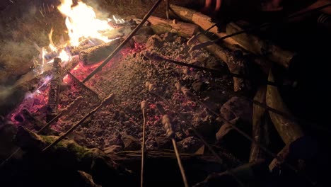 Baking-bread-on-wooden-sticks-over-campfire-at-night-in-camp,-close-up,-static-shot