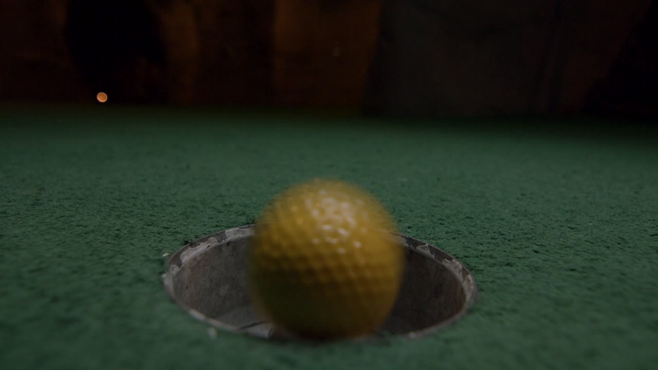 una mini pelota de golf amarilla cae en el hoyo de golf y rebota en el bolsillo de un campo